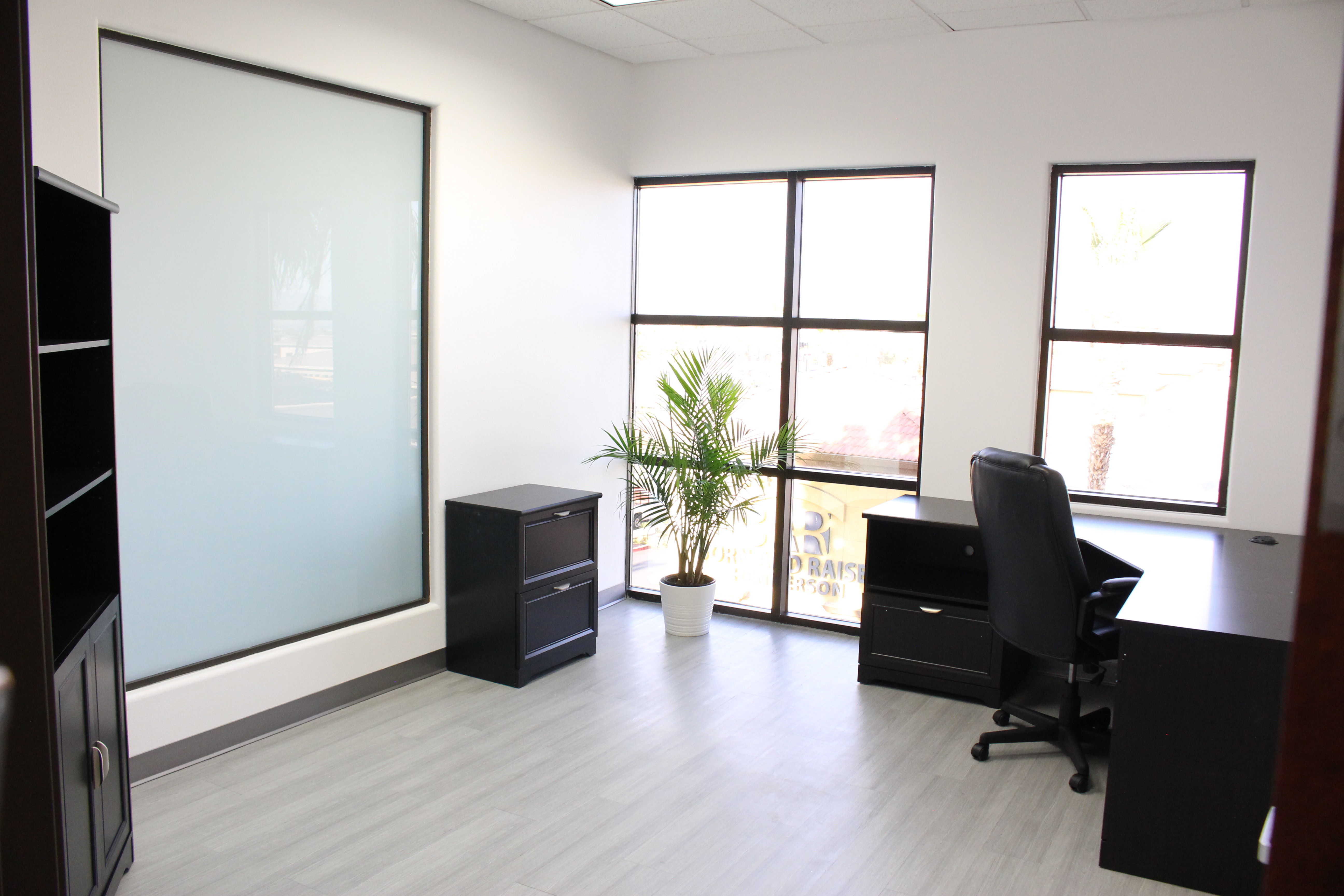 A large office space with two big widows, a filing cabinet, l-shaped desk and chair.